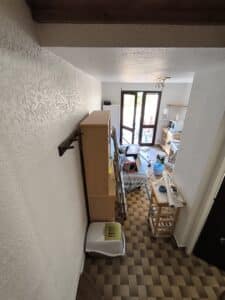 Espace de vie avec mur texturé, meuble bois, litière pour chat sur sol carrelé. Vue sur réfrigérateur, micro-ondes et porte-fenêtre.