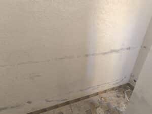 Mur texturé beige avec des lignes d'humidité ou de réparation horizontales et un sol carrelé sale de rénovation.