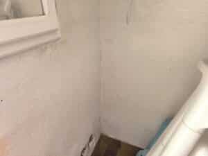 Mur blanc texturé avec humidité et moisissures près d'une fenêtre et prises électriques. Sol carrelé. Signes de dégâts des eaux.