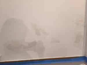 Mur clair avec peinture écaillée et zones de plâtre apparentes, signes d'humidité ou réparation inachevée. Bande de protection bleue au bas.