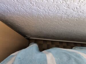 Plafond blanc texturé au-dessus d'un meuble en bois, un sol carrelé et une couverture rayée bleu et blanc en premier plan.