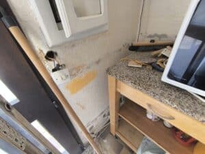 Mur texturé avec dégâts d'eau, interrupteur électrique, balai, et un "Smart Oven" blanc sur un comptoir en granite.