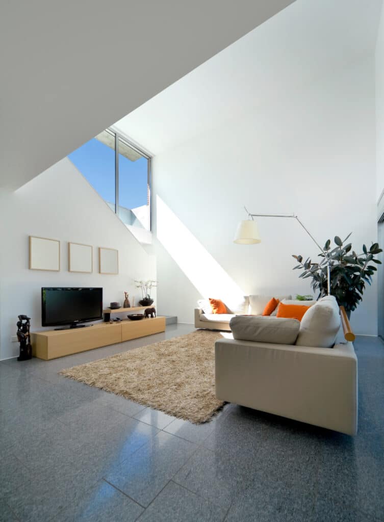 Salon moderne et lumineux avec canapés crème, TV, tapis shaggy beige sur carrelage gris. Grandes fenêtres et lumière naturelle intense.